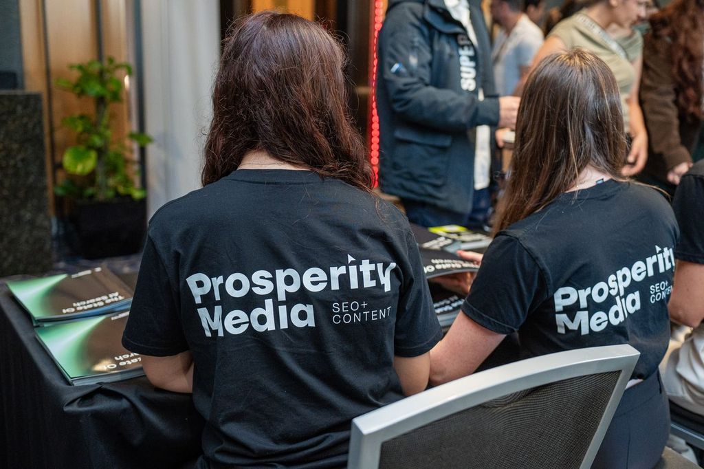 Two Prosperity Media team members at an event table with State of AI Search booklets